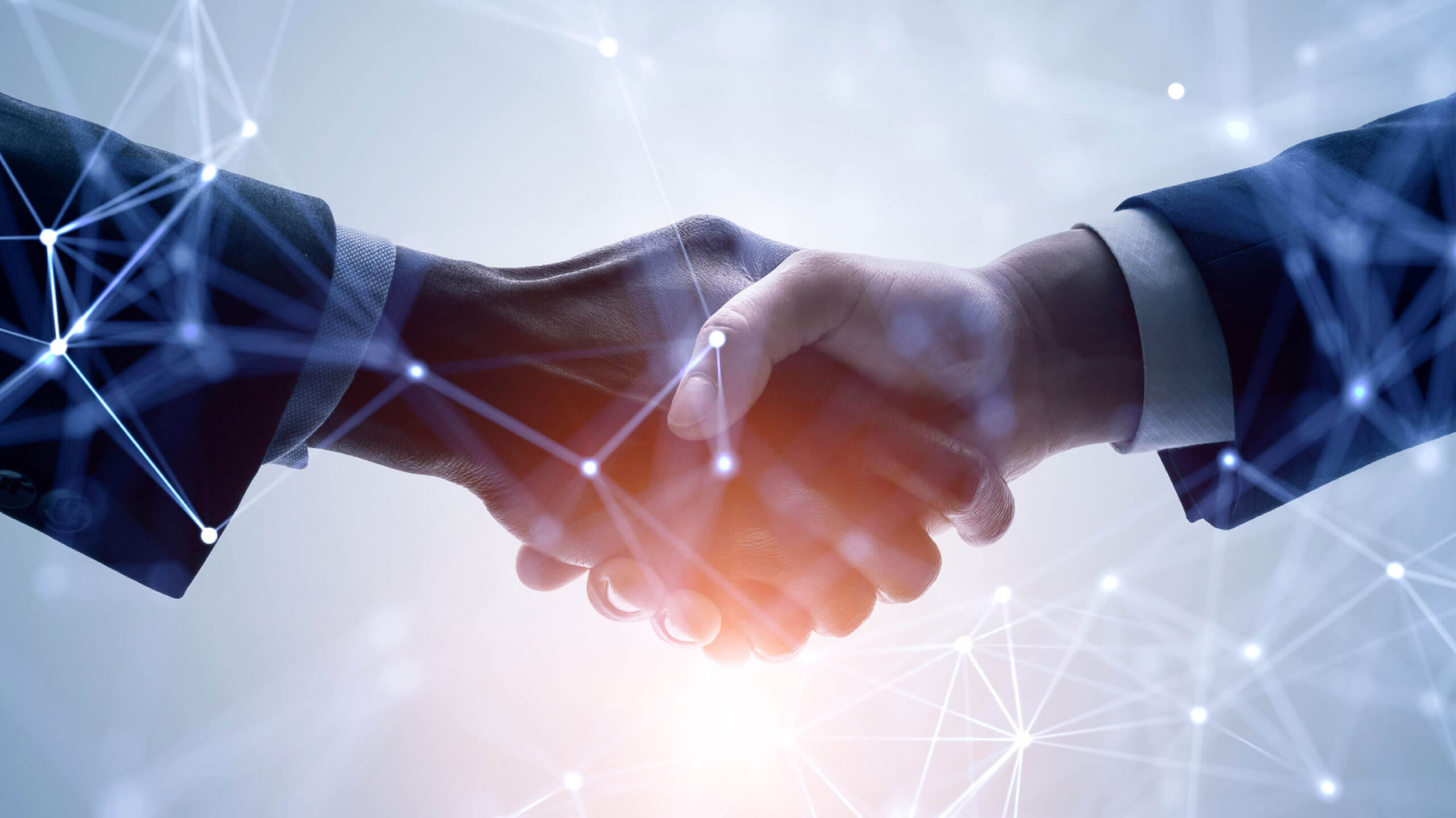 Zwei Personen in Businesskleidung schütteln sich die Hand vor einem hellen, abstrakten Hintergrund. Über das Bild sind leuchtende Linien und Knotenpunkte gelegt, die ein Netzwerk oder ein digitales Verbindungsgeflecht darstellen. Ein warmes Licht scheint von unten auf die Hände.