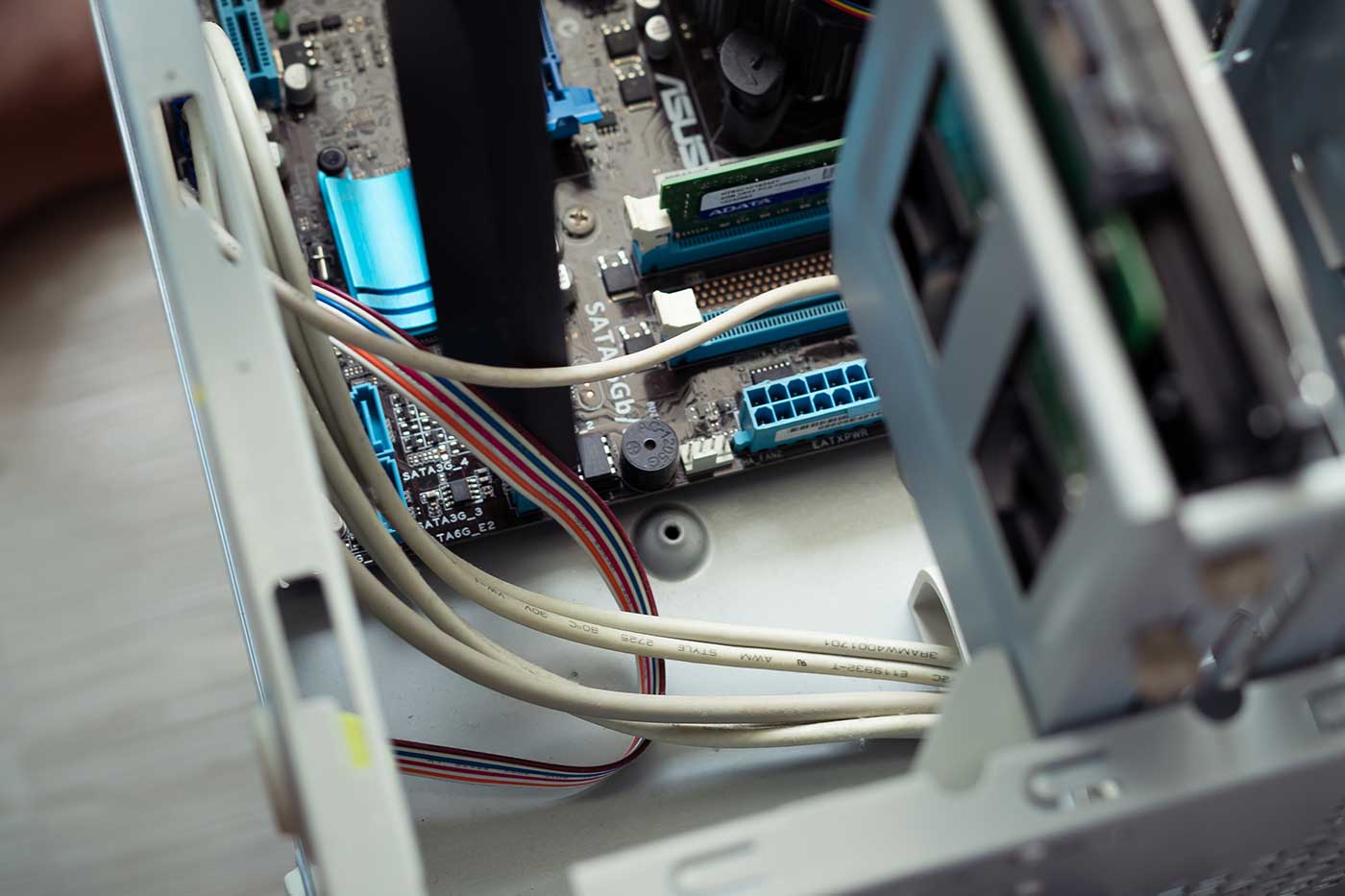 Blick ins Innere eines geöffneten Computergehäuses. Sichtbar sind Kabel, ein Mainboard mit eingebauten RAM-Riegeln sowie verschiedene Steckverbindungen und Bauteile. Im Vordergrund verläuft eine Gruppe von Daten- und Stromkabeln. Die Aufnahme zeigt Details der Computerhardware.