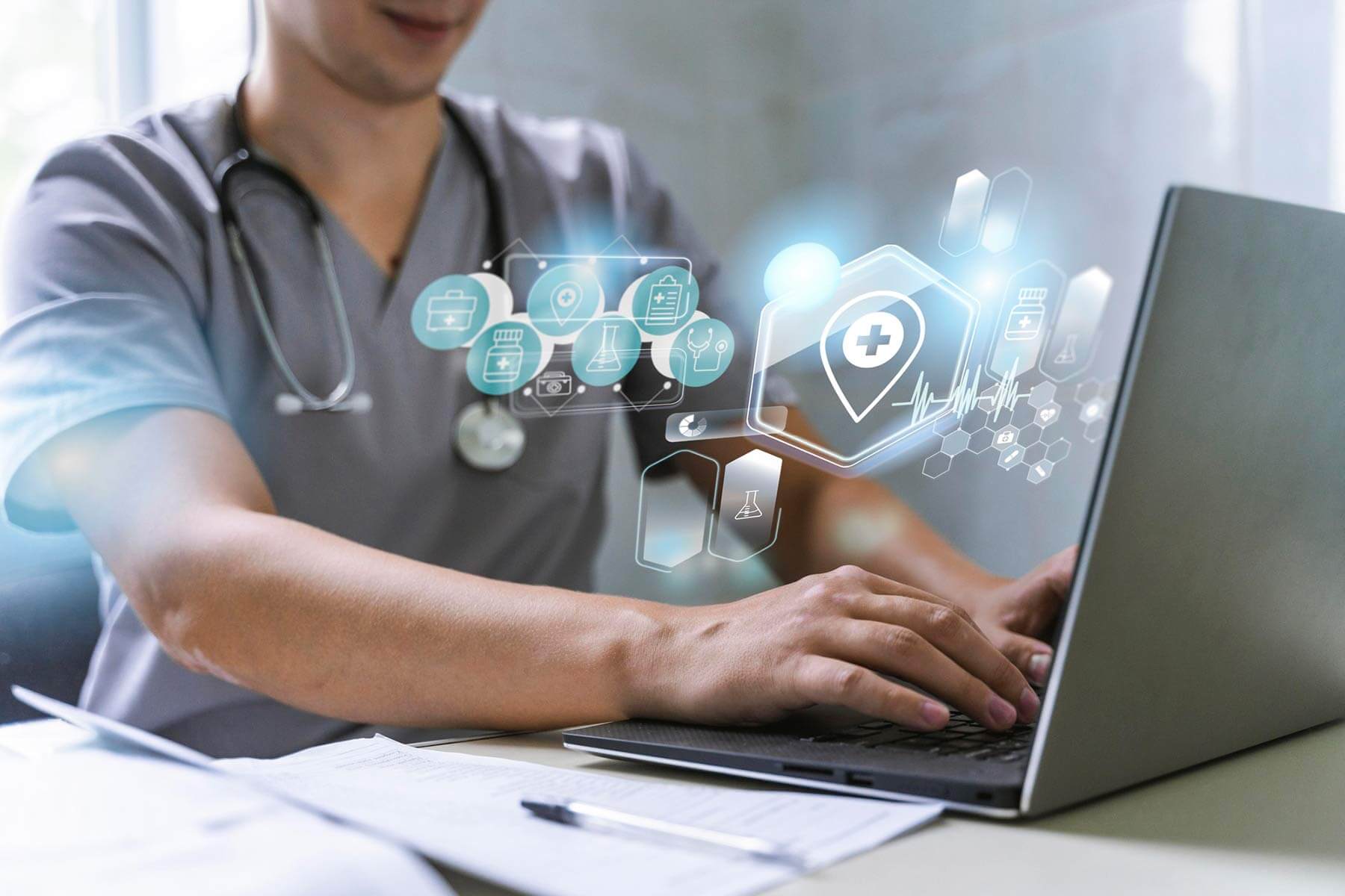 Eine Person in medizinischer Kleidung mit Stethoskop arbeitet an einem Laptop. Über dem Laptop sind digital eingefügte Symbole zu medizinischen Themen eingeblendet. Auf dem Tisch liegen Dokumente und ein Stift.